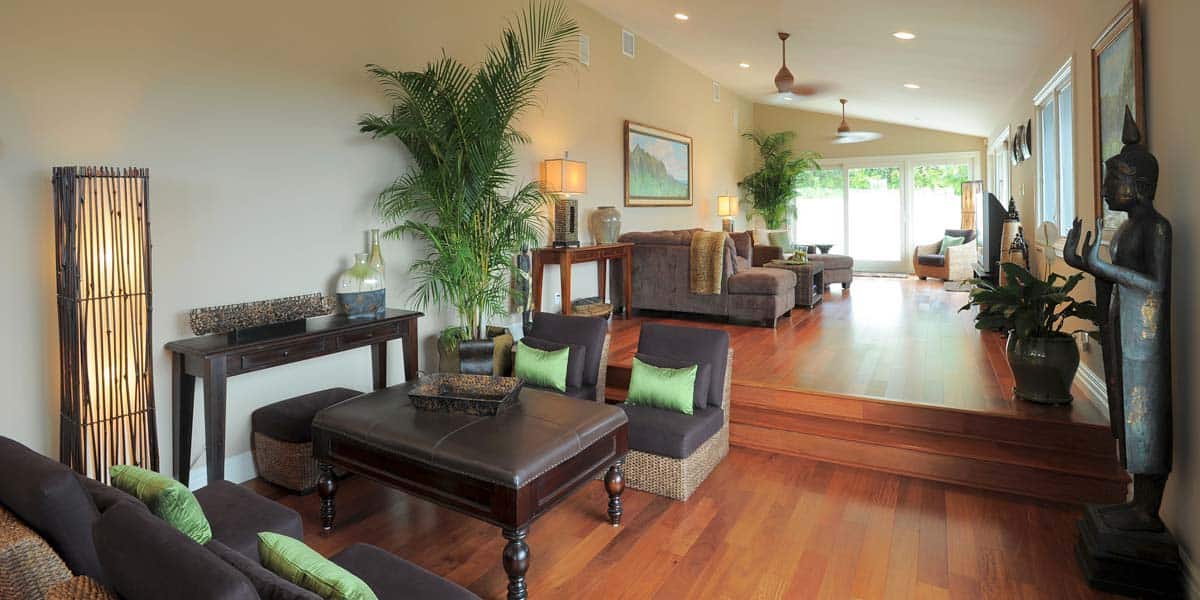 Spacious living room with wooden floors, tropical plants, modern furniture, decorative lamps, and a large Buddha statue near a sunlit window—an ideal setting reflecting Oahu Home Remodeling style.