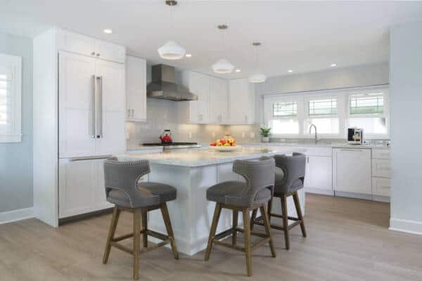 Modern kitchen in Oahu with white cabinets, stainless steel appliances, an island with gray chairs, pendant lights, and wooden flooring—perfect for your remodeling inspiration. A bowl of fruit and a coffee maker add charming touches.